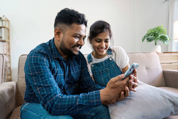 istock Happy Indian Couple Relaxing at Home and Using Smartphone Together on Couch 2160689825