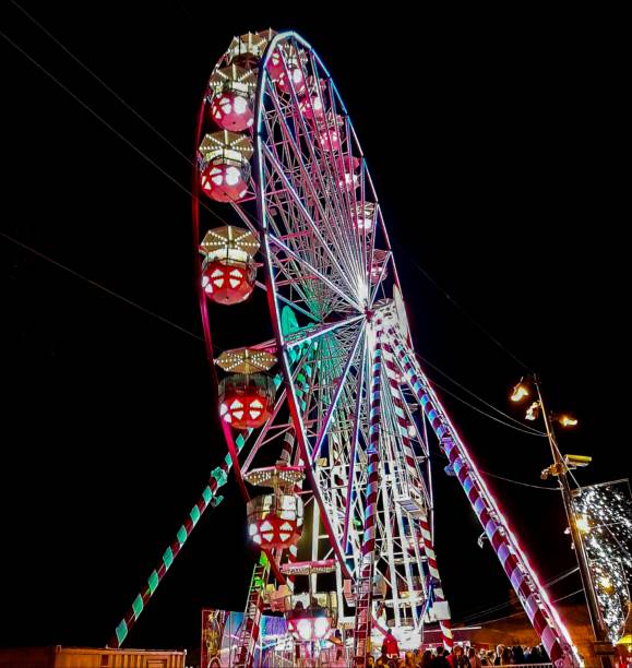 Experience the magic of a brightly lit Ferris wheel against the night sky. Captured in stunning detail, this photo showcases the vibrant colors and illuminated gondolas, creating a mesmerizing scene at a nighttime fair. Perfect for carnival enthusiasts and lovers of nighttime photography.