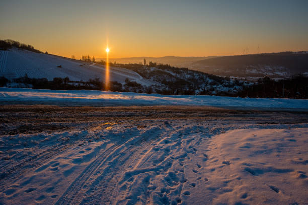 Road with snow in winter vineyard landscape and back lit