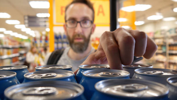 Close-up of many aluminum cans of beer in a store fridge and a male buyer taking one A male buyer takes a can of alcohol drink from a ftore fridge grocery shelf cans stock pictures, royalty-free photos & images