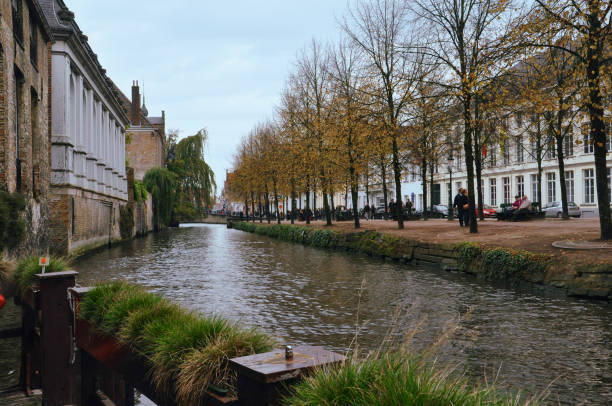 30-10-2014 Brussels, Belgium - A serene canal in Bruges with tree-lined paths and people enjoying a peaceful walk