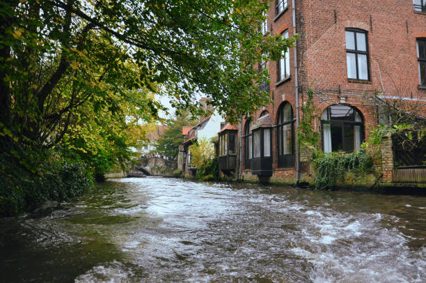 30-10-2014 Brussels, Belgium - Traditional houses, tourists, and bridges line Bruges canal viewed from a boat