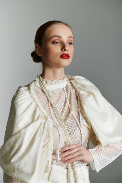 istock Woman in white blouse with pearls against gray backdrop. 2160709575