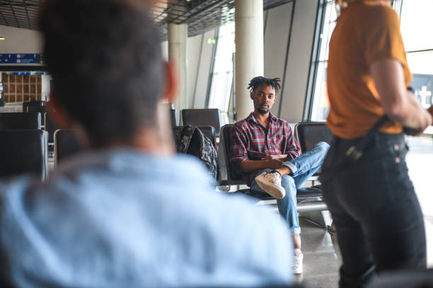 Latin young adult male sitting in the airport lobby waiting for his flight using smartphone.
