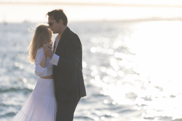 A couple dances on a beach as the sun sets, casting a golden glow over the water.
