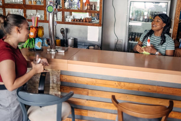 Waitress working inside of cafe cleaning bar counter while talking to a friend