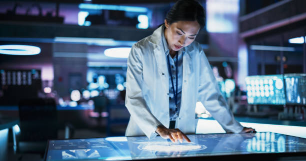 istock Female Asian Neuroscinetist Using Interactive Touch Screen Table With MRI Scans On Display In Modern Biotechnology Research Center. Doctor Developing Innovative Devices For People With Brain Damage. 2160715513