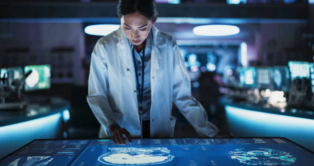 istock Female Asian Neuroscinetist Using Interactive Touch Screen Table With MRI Scans On Display In Modern Biotechnology Research Center. Doctor Developing Innovative Devices For People With Brain Damage. 2160715542