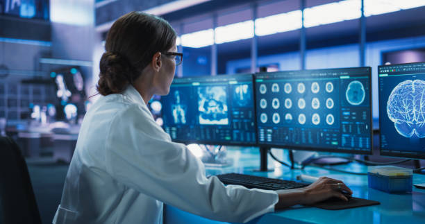 istock Hospital Research Laboratory: Female Medical Scientist Using Computer with Brain Scan MRI Images. Professional Neurologist Analysing CT Scan, Finding Treatment Solutions for Patient With Brain Damage. 2160716927