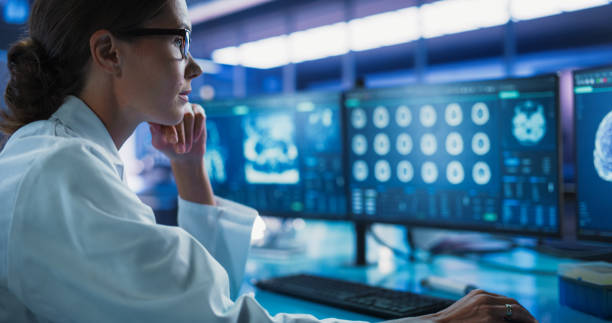 istock Hospital Research Laboratory: Female Medical Scientist Using Computer with Brain Scan MRI Images. Professional Neurologist Analysing CT Scan, Finding Treatment Solutions for Patient With Brain Damage. 2160716955