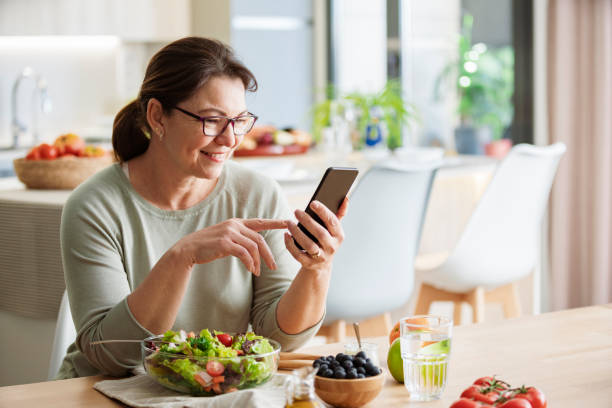 istock Woman is sitting at the table using mobile phone while having healthy vegetables meal 2160717018