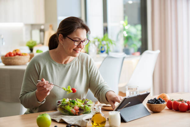 Woman is sitting at the table using digital tablet while having healthy vegetables meal