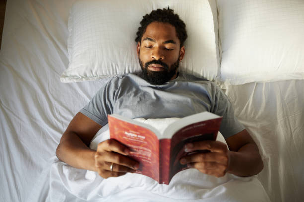 Above view of relaxed black man reading a book in bed.