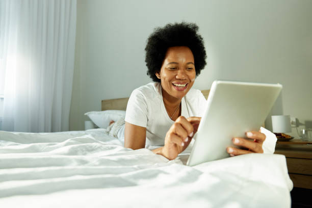 istock Happy black woman using touchpad on a bed in bedroom. 2160718004