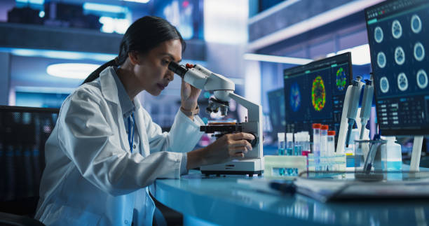 istock Medical Research And Development Center: Female Asian Scientist Using Microscope To Analyze Petri Dish Sample. Specialist Developing Innovative Medicine For Treating Mental Disorders Or Pain Relief. 2160720369