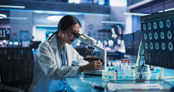 istock Medicine Development Laboratory: Asian Female Scientist Using Microscope, Analyzes Petri Dish Sample. Big Pharmaceutical Lab with Specialists Conducting Biotechnology Research, Developing New Drugs. 2160720388