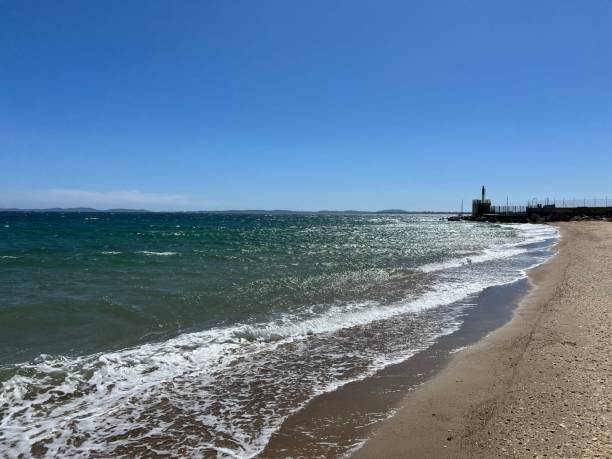 istock Serene beach scene with gentle waves and a clear blue sky, featuring a distant lighthouse 2160720698