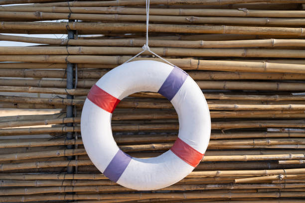 A white and red life preserver is hanging from a bamboo fence. The life preserver is upside down and he is upside down