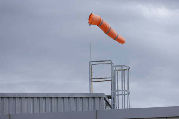 A large orange kite is flying in the sky above a metal structure. The kite is attached to a metal pole and is flying high in the air. The sky is cloudy