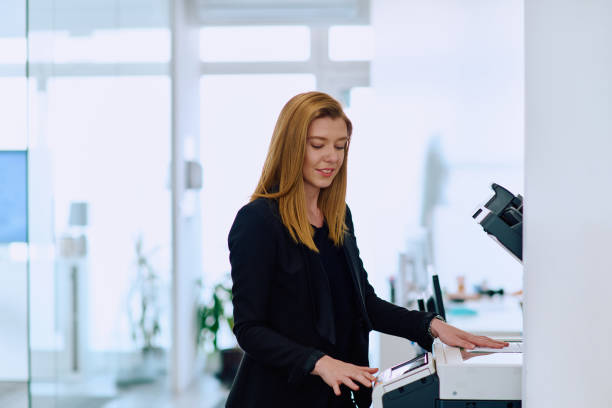 istock Blonde Businesswoman Using Printer in Office Setting. 2160730220