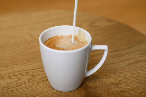 Detailed close-up from above of an old-fashioned white porcelain mug filled with freshly poured black coffee, with milk and a bit of foam on the side. the background is white with a soft shadow gradient to the right. the handle is on the left. This photo also contains a clipping path
