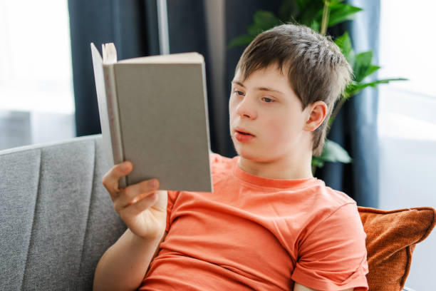 Teenager with down syndrome reading a book on a sofa