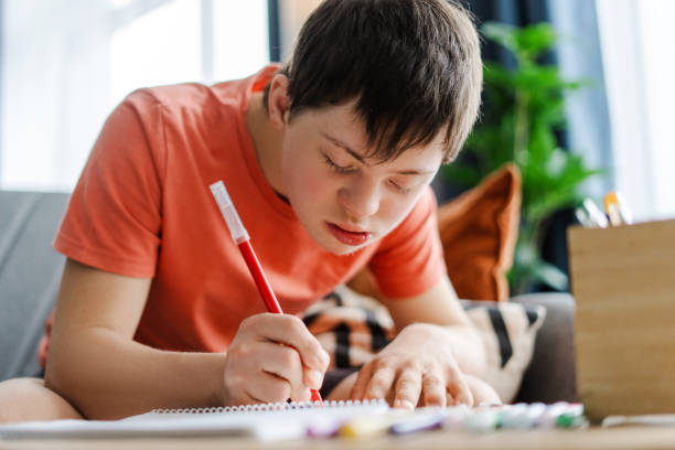 istock Young boy with down syndrome drawing in notebook at home closeup 2160736654