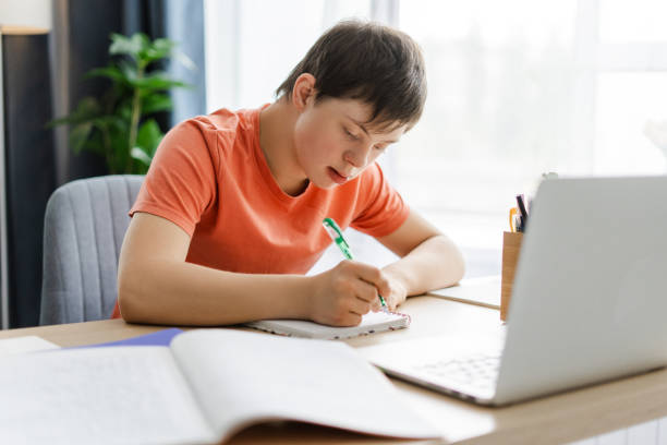 istock Young student with down syndrome is studying at home using laptop, sitting at home 2160736689