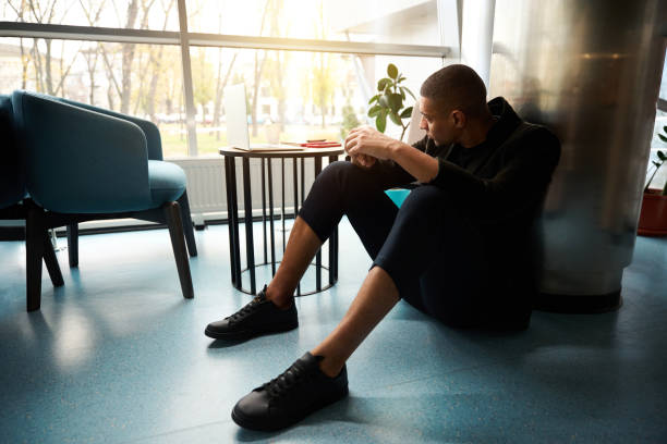 istock Sad guy sitting on floor and looking through window 2160738043
