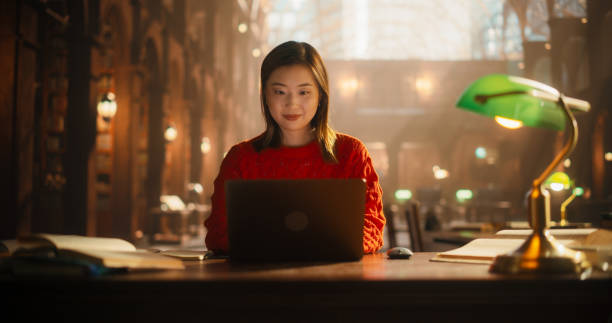 istock Dedicated Asian Female Student Engaged in E-Learning With Laptop in Classical Library. Young Woman Focused on Digital Study, Surrounded by Books and Classical Architecture. 2160741790