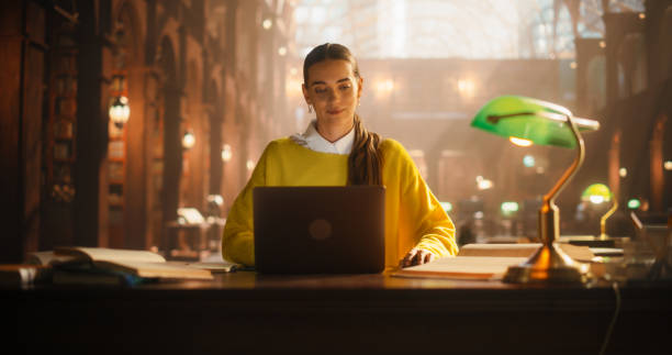 istock Engaged Young Woman Studying in a Classical Library Setting. Female Student Using Laptop for E-Learning Amidst Rows of Books, Focused on Academic Research and Online Education. 2160741841