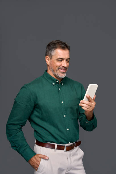 istock Smiling mature businessman using cell phone isolated on gray background. 2160741887