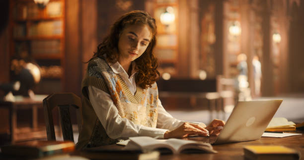 istock Serene Young Woman Engaged in Studying With Laptop and Books in a Classical Library Setting, Surrounded by Wooden Shelves Filled With Books, Illuminated by Warm Ambient Light 2160742169