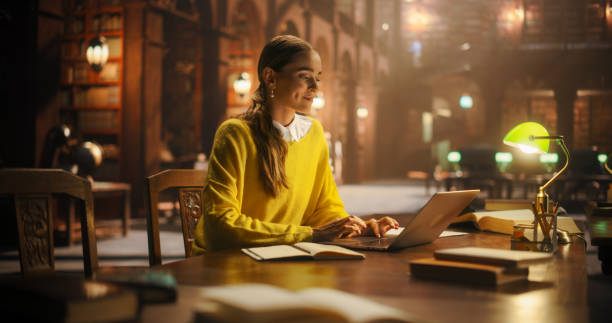 istock Thoughtful Multiethnic Asian College Student Using Laptop Computer to Study in a Classic Library. Beautiful Young Woman Learning Online, Getting Ready for Exams, Taking Notes and Drafting an Essay. 2160742859