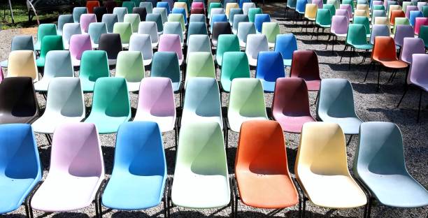 istock Rows of empty colorful plastic chairs geometrically arranged with side sunlight. 2160744571