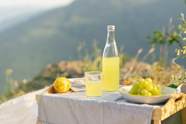 A serene summer picnic scene with lemonade, a lemon, and grapes on a table, set against a natural backdrop