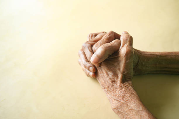 An elderly woman in mourning clothes clasping her hands together