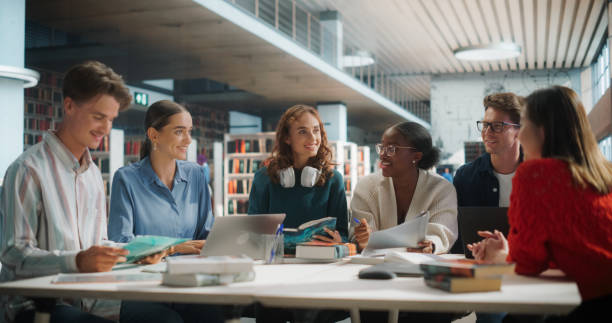 istock Diverse Group of Students Collaborating on a Project in a Modern Library. Young Men and Women Using Laptops and Books, Engaging in Group Discussion and Learning Together. 2160751348