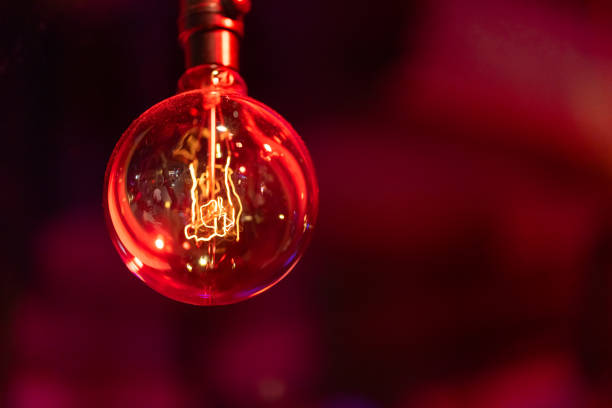 Close-up of a glowing red light bulb with visible filament. The artistic image highlights the warm, moody atmosphere of the setting.