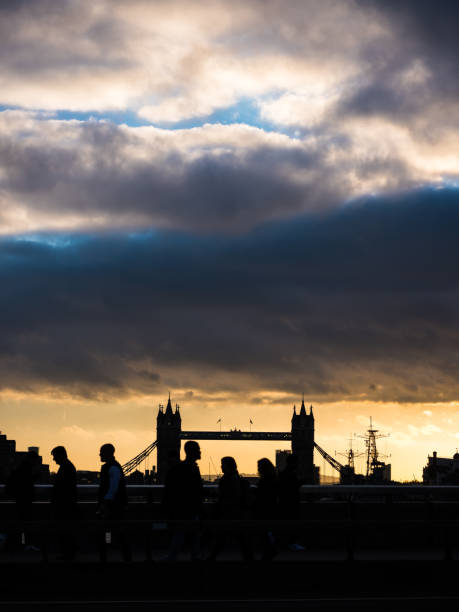 Crowds of commuters on London Bridge silhouetted against the iconic battlements of Tower Bridge over the River Thames in  central London, UK.