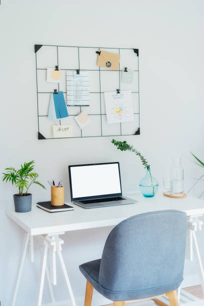 istock Modern Contemporary workplace design. White desk with laptop mockup empty screen, grid mood board with pinned notes and plans, green plants, office supplies at work space in home office room interior 2160765555