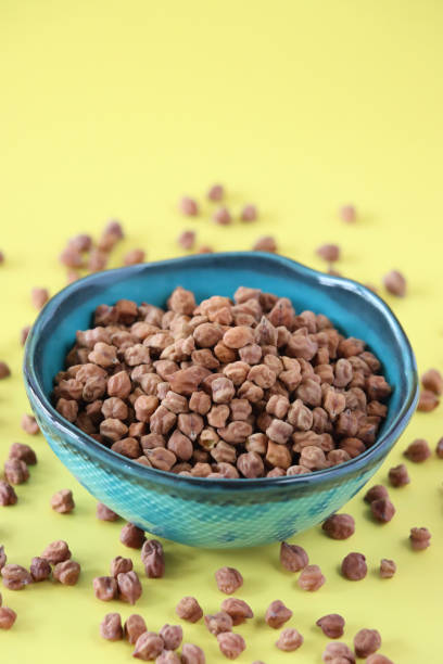 istock Image of dried bengal gram black chickpeas in blue ceramic bowl, surrounded by scattered lentils and pulses, healthy food, against yellow background 2160776722