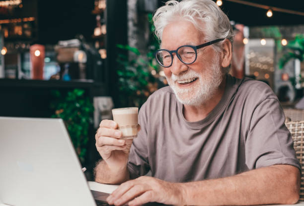 istock An elderly man enjoying a coffee cup in a cafe, smiles while using his laptop on a video call. Cheerful senior male, highlighting happiness and contentment in a relaxed atmosphere 2160793132