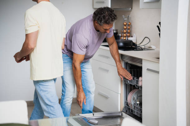 istock Mature man putting dishes away in a dishwasher with partner passing by 2160802377