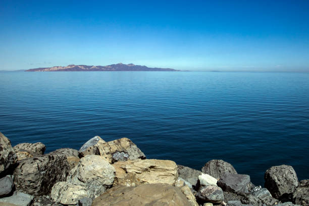 Island as seen from the Great Salt Lake State Park, clear blue sky with a single cloud over the island, large boulders in the foreground.