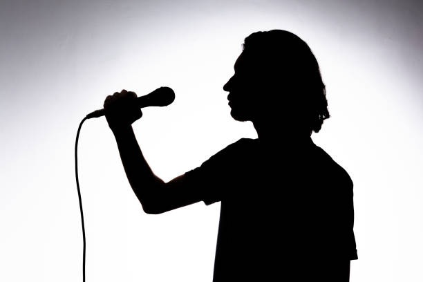 istock Silhouette of young singer holding wired microphone and singing with emotion. 2160804829