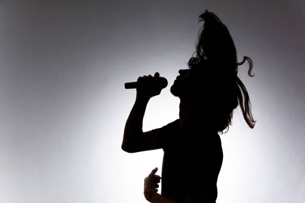 istock Silhouette of young man holding wireless microphone singing music with emotion. 2160804833