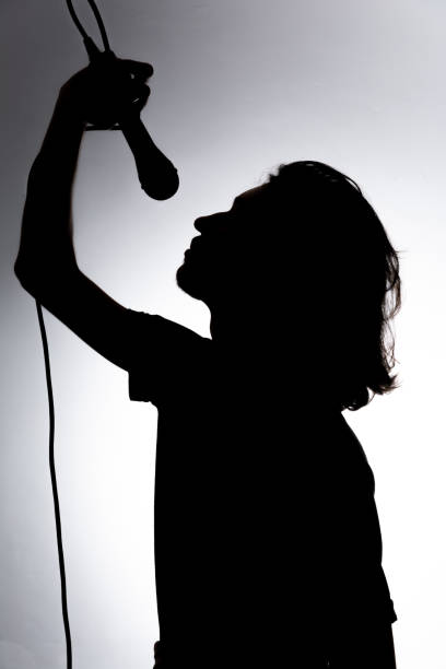 istock Silhouette of young singer holding wired microphone and singing with emotion. 2160804836