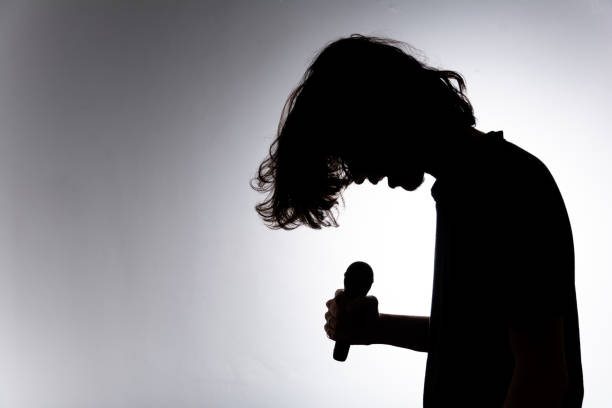 istock Silhouette of young man holding wireless microphone singing music with emotion. 2160804842