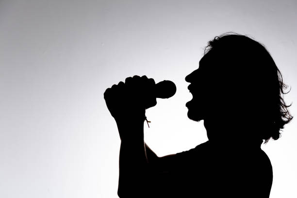 Silhouette of young man holding wireless microphone singing music with emotion. Isolated on white background.